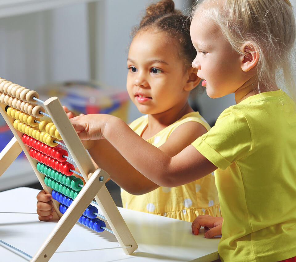 Two children play together with a colorful abacus, exploring numbers and colors during a fun learning activity in a bright classroom.