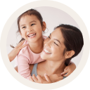 A woman gently holds a young child on her shoulder, both smiling.