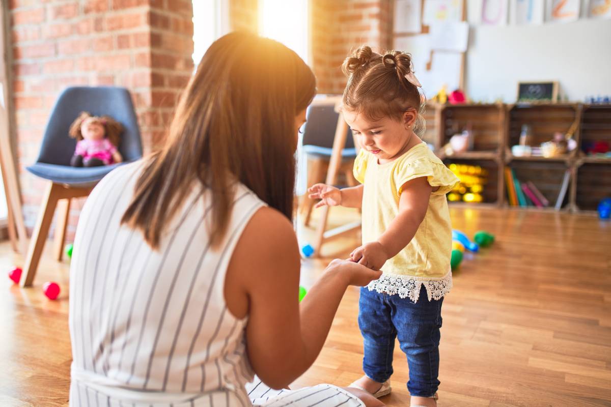 Young teacher and toddler playing with small building blocks toy at kindergarten